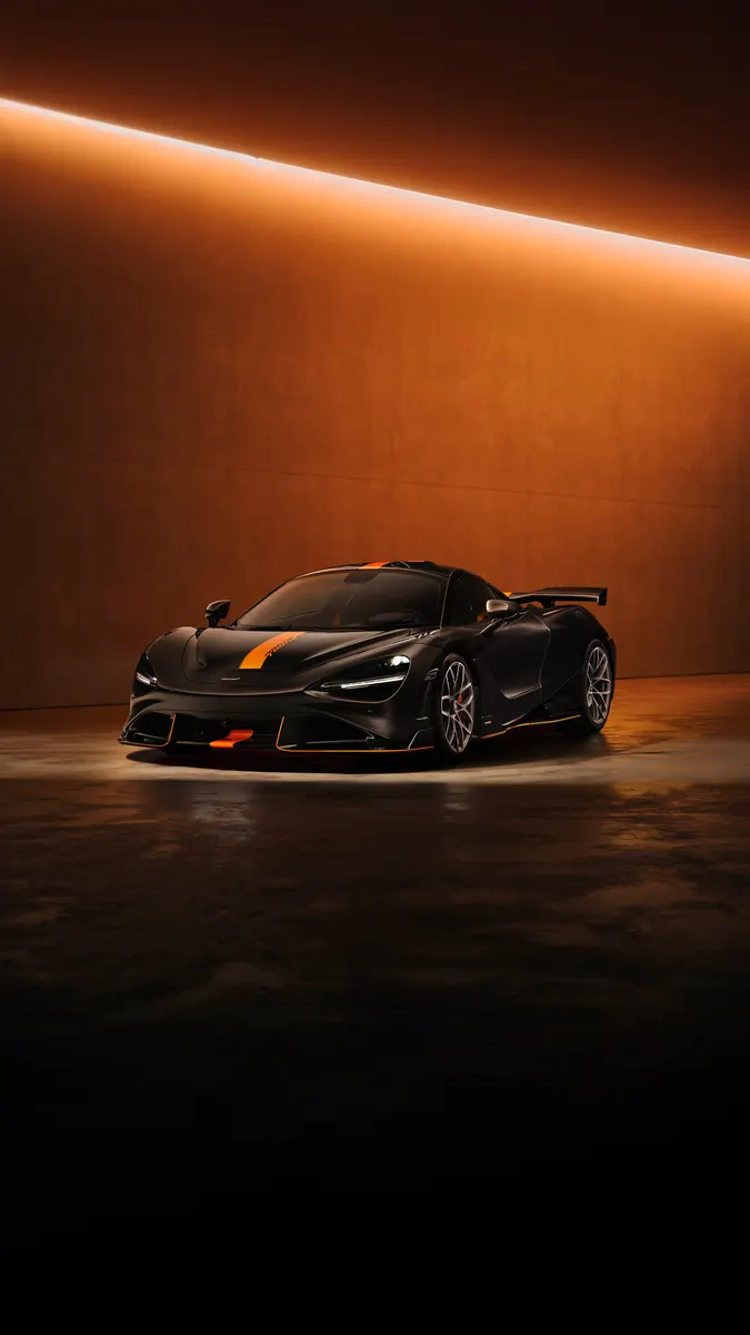 A black McLaren sports car with orange accents is parked in a dark studio with warm orange lighting.